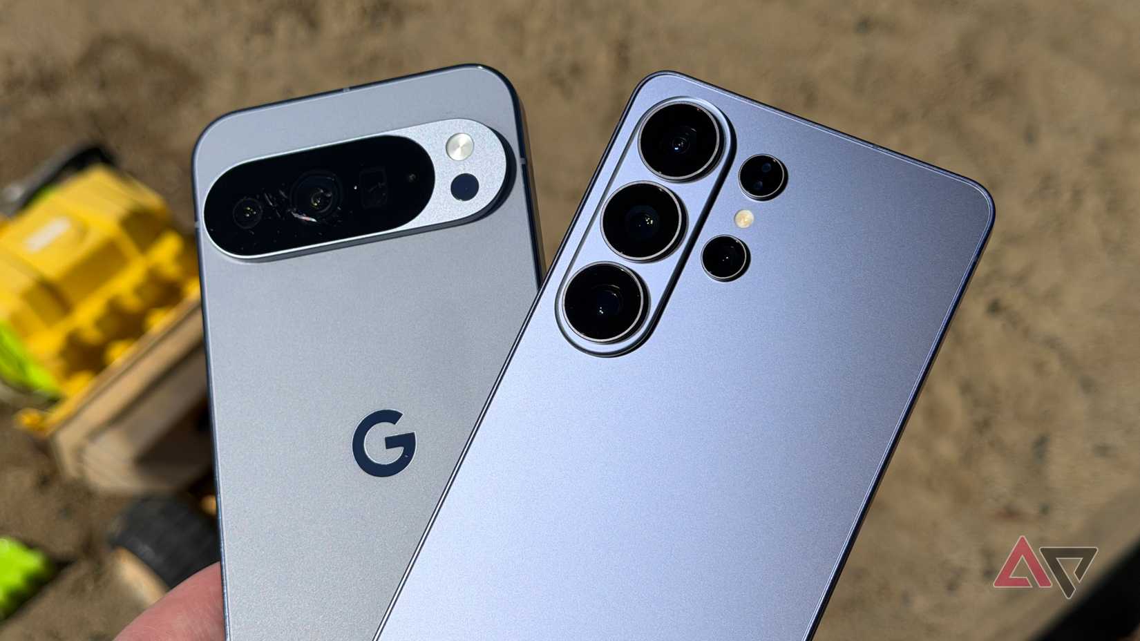 Galaxy S26 Ultra and Pixel 10 Pro XL held on a sunny day over a sandbox
