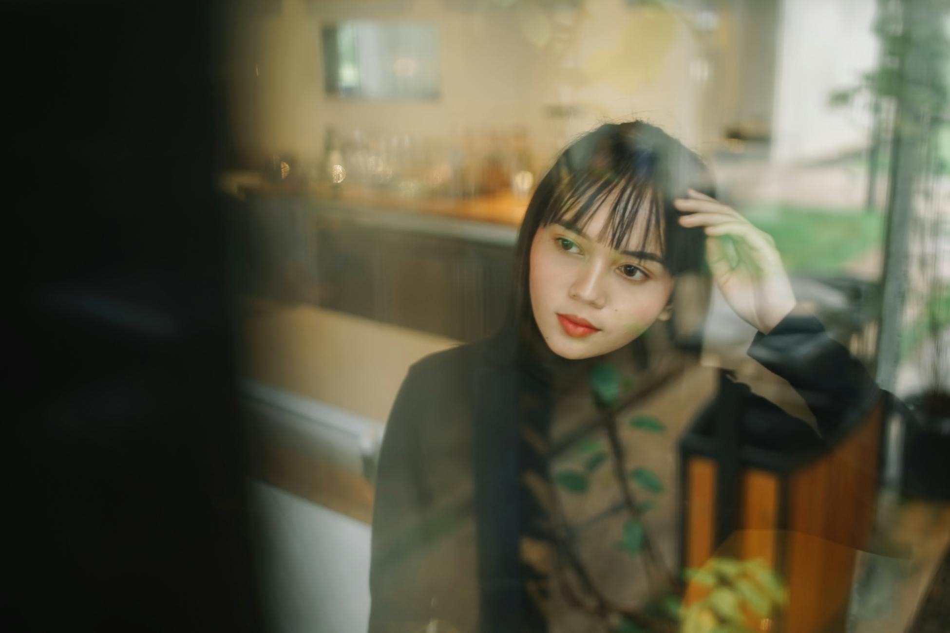 A thoughtful woman reflects while sitting inside, viewed through a window.