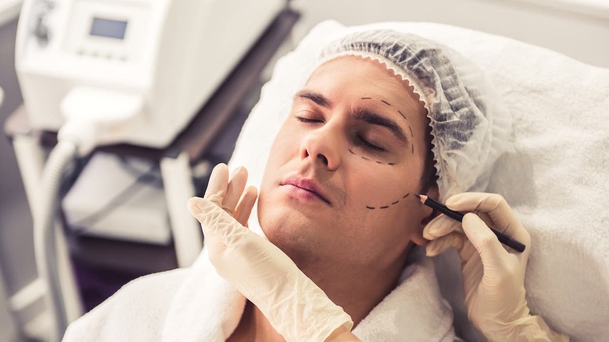 Handsome man sitting while doctor in medical gloves examines his face with a pencil