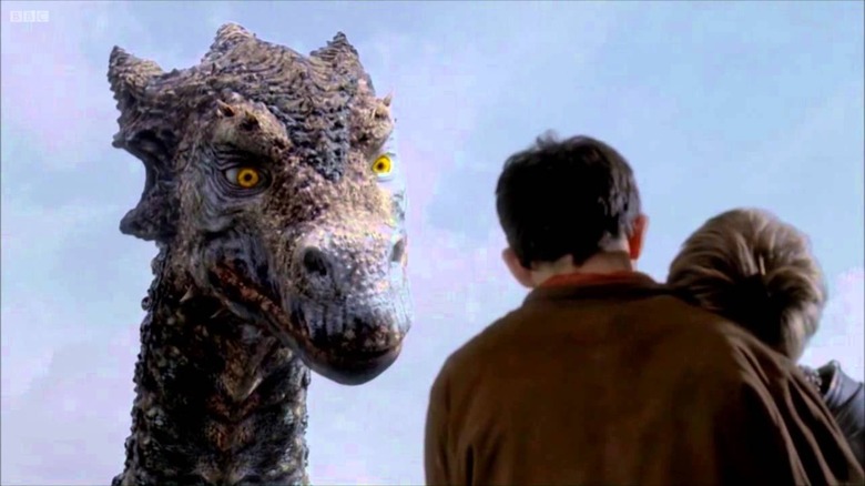 Merlin (Colin Morgan) holds a woman as he heeds the words of the great dragon, Kilgharrah (John Hurt) on 