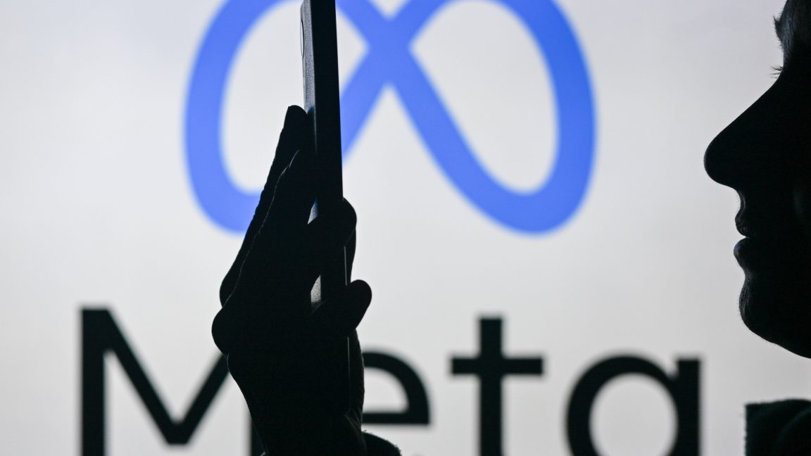 An image of a woman holding a cell phone in front of the Meta logo displayed on a computer screen.