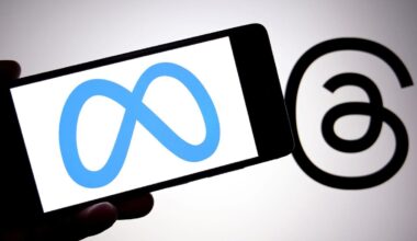 A blue Meta logo on white background on a mobile phone is held next to a black Threads logo.