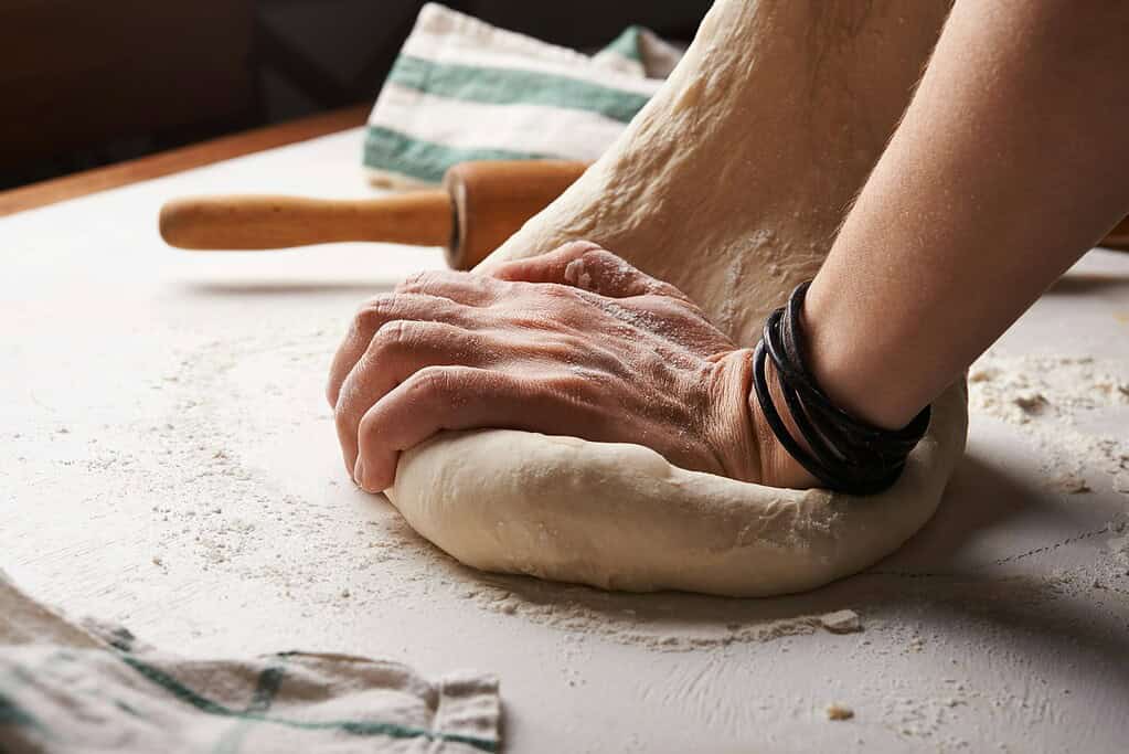 Person kneading dough for baking on a floured surface.