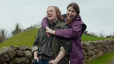 Two people embrace and laugh as they walk along a country lane. 