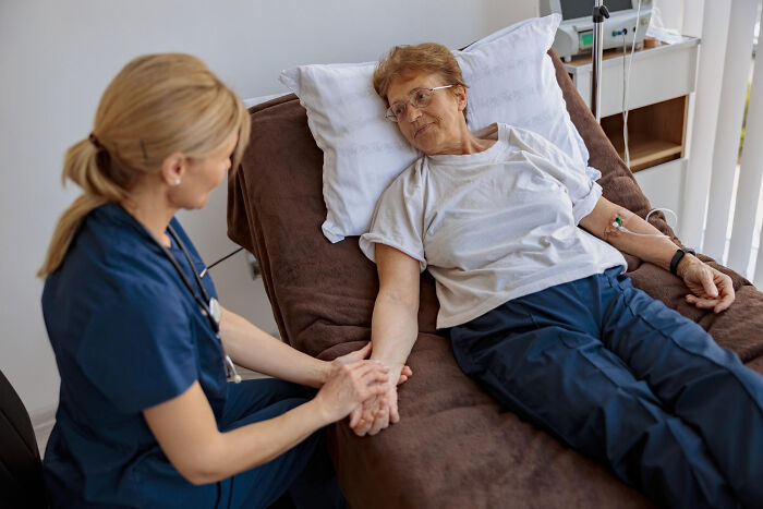 Surgical staff comforting elderly patient reclining on hospital bed during sedation and treatment in clinical setting.