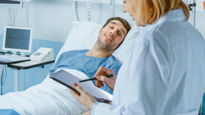 Surgical staff talking with a patient in hospital bed, documenting unusual patient confessions under sedation.