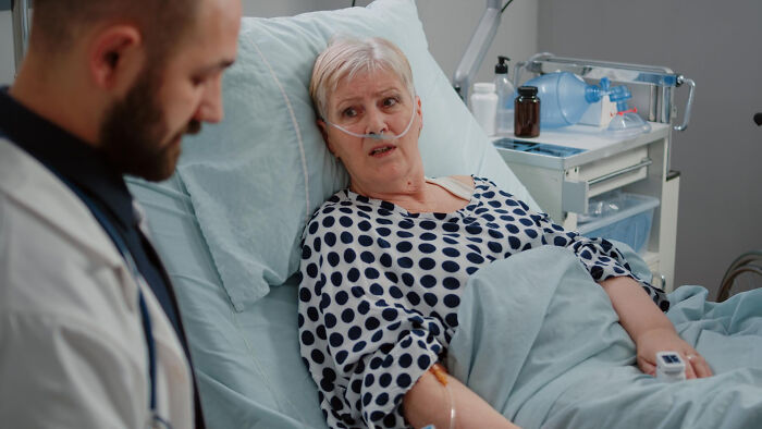 Elderly patient in hospital bed with nasal oxygen, talking to surgical staff during sedation and medical care.