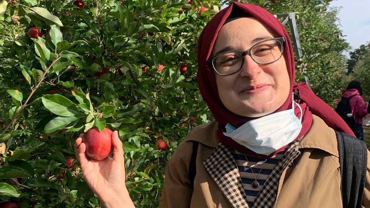 Rumeysa Ozturk standing outdoors holding apples during an apple-picking trip