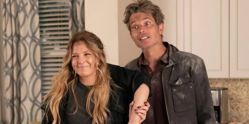 Sheila and Joel smiling and covered in dirt as Sheila holds a severed arm in Netflix's Santa Clarita Diet.