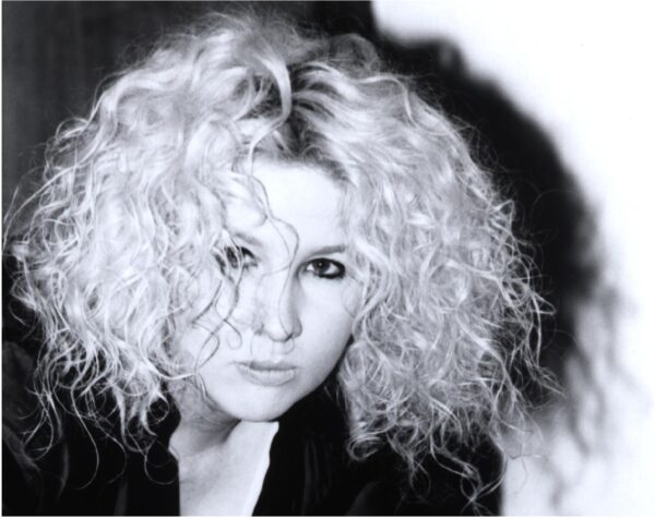 A young woman with lots of curly, medium-length blonde hair and dark eye makeup.