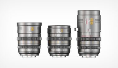 Three professional camera lenses of varying heights are displayed upright side by side against a white background. Each lens has a metallic finish with engraved numbers and markings in yellow, orange, and white.