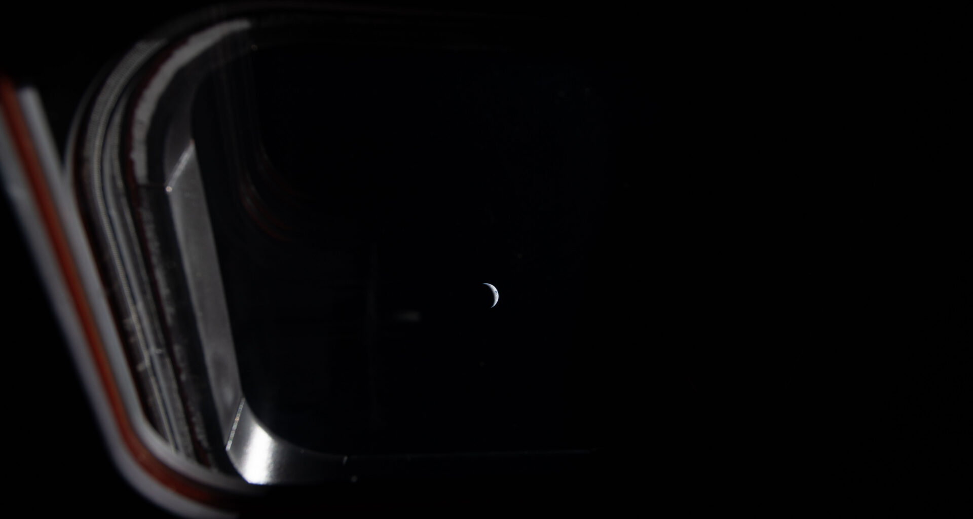 Peering out one of the four windows near the display console on the Orion spacecraft, the Earth is illuminated by the blackness of space and grows smaller as the crew journeys closer to the Moon. This image was taken by an Artemis II crew member on the fifth day of the mission.