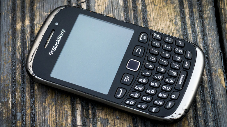 A scracthed Blackberry phone with a physical keyboard against a weathered wood background