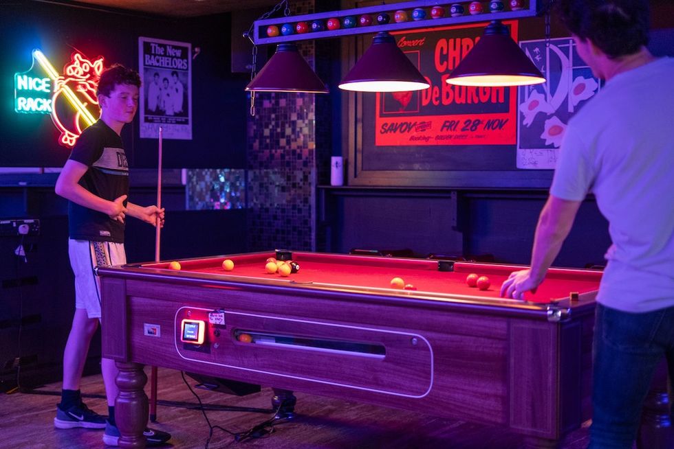 Two people playing pool in a neon-lit room at Level Up Arcade with posters on the walls.