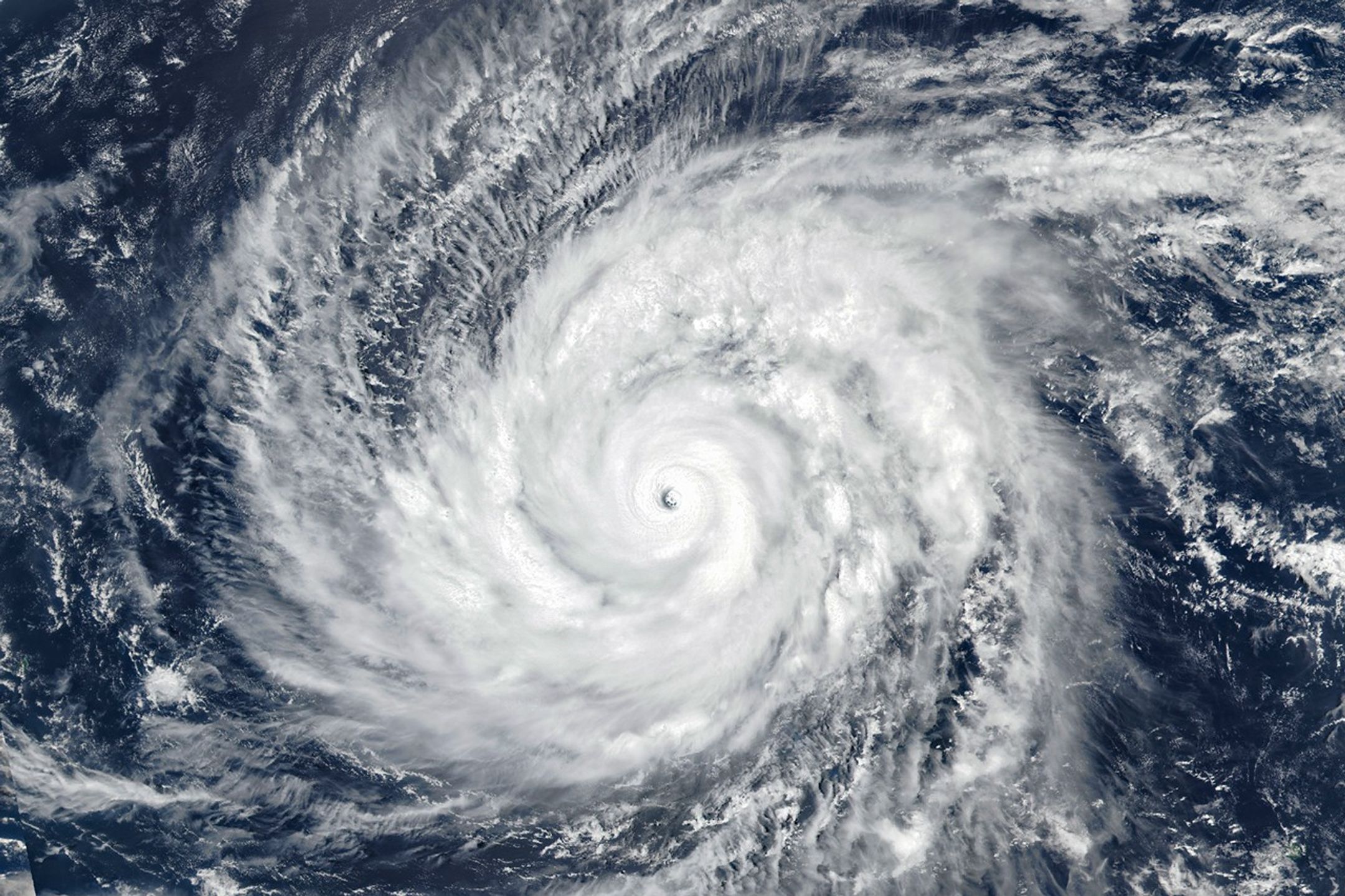A large tropical cyclone spins over blue ocean water, its bright white cloud bands extending across parts of the Mariana Islands.