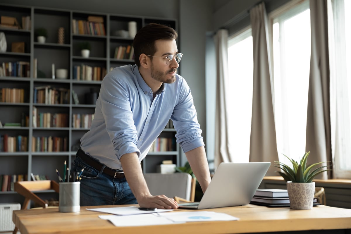 An investor leans against a desk and looks pensively out a window.