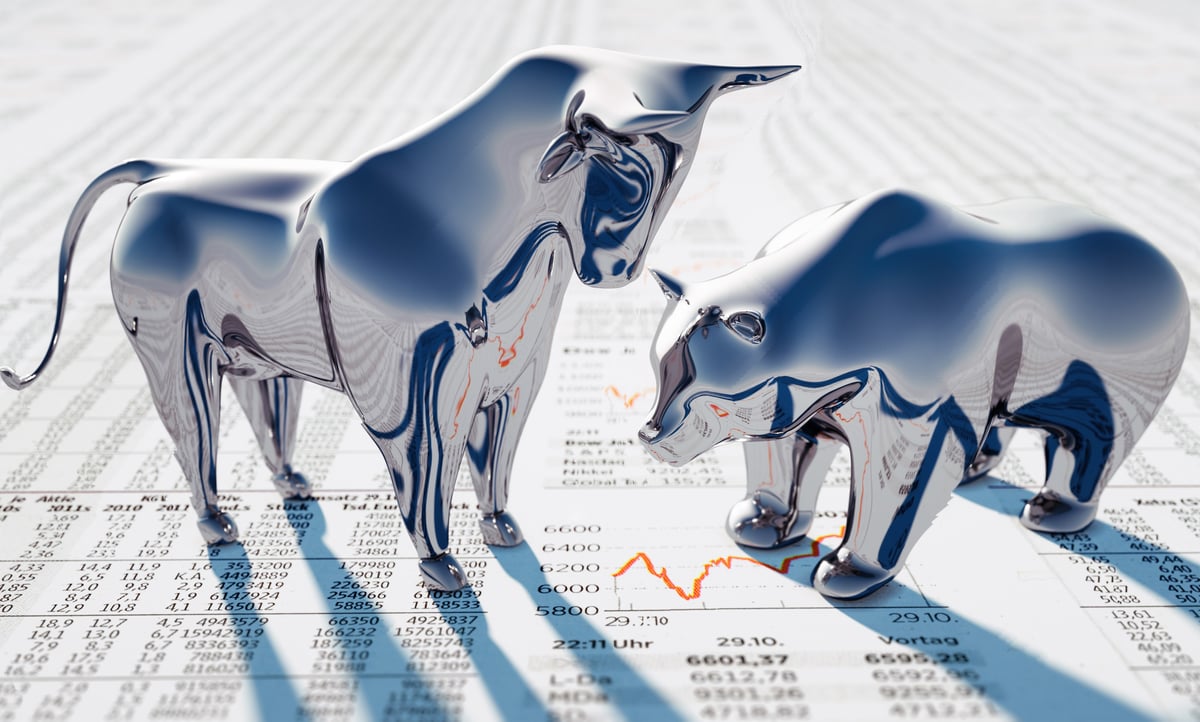 A silver bull towers over a silver bear, both of which stand on newsprint.