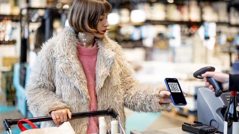 Woman pays with a QR code or scans her loyalty card on phone at a supermarket checkout.