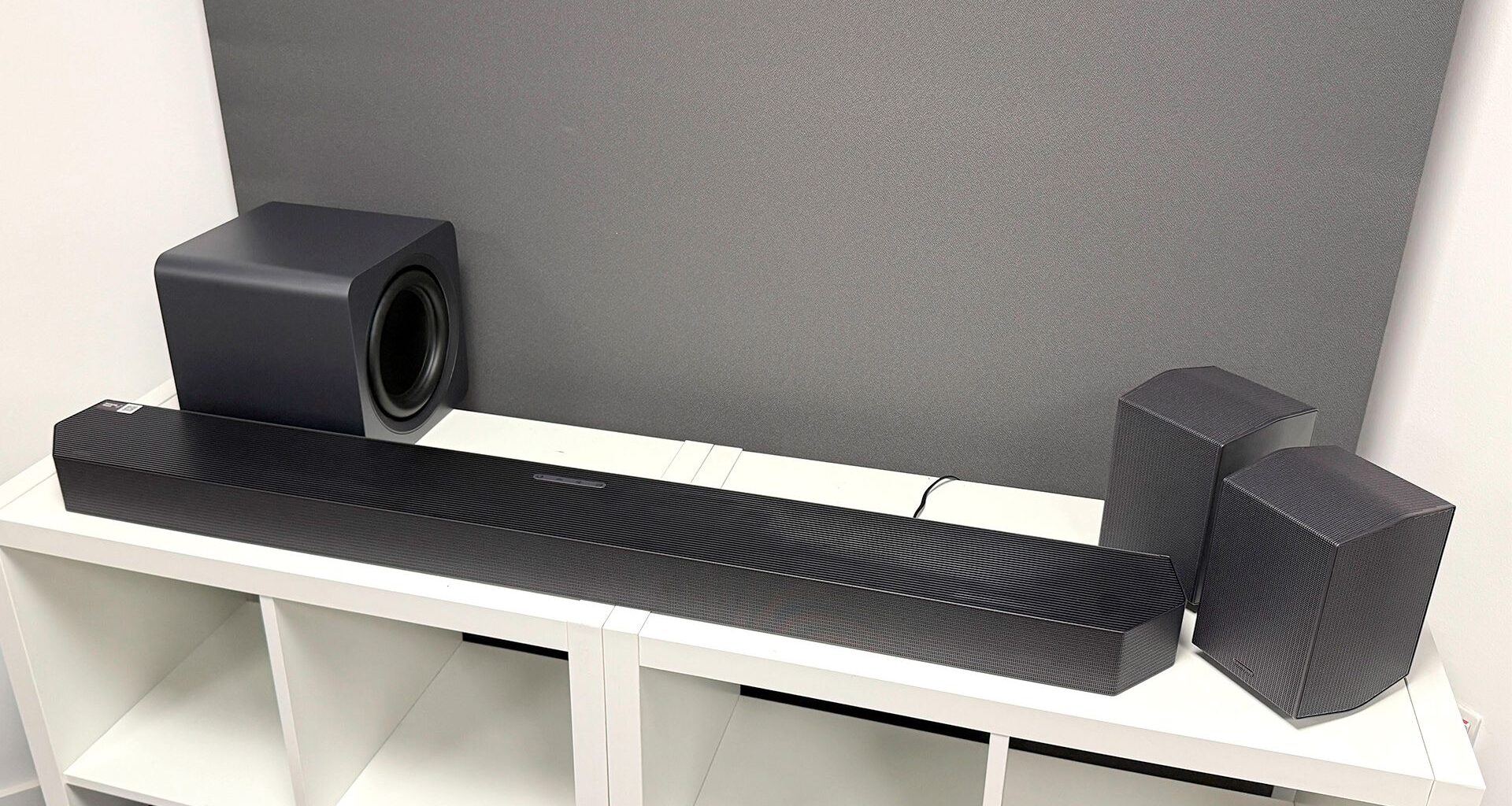 Samsung HW-Q990H soundbar package on white wooden shelf unit in front of grey baffle
