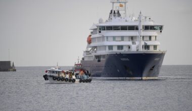 A small boat travels away from the side of a large cruise ship in open water.