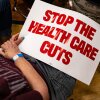 An attendee holds a "Stop The Health Care Cuts" sign during a June 6 town hall hosted by Michigan Democrats in Lansing. In July, Congressional Democrats failed to stop Republicans from passing a tax-and-spending bill that mandated that 40 states and the District of Columbia institute work requirements for Medicaid eligibility. Michigan launched a system for verifying work requirements in 2020, but shut it down after a court ruling.