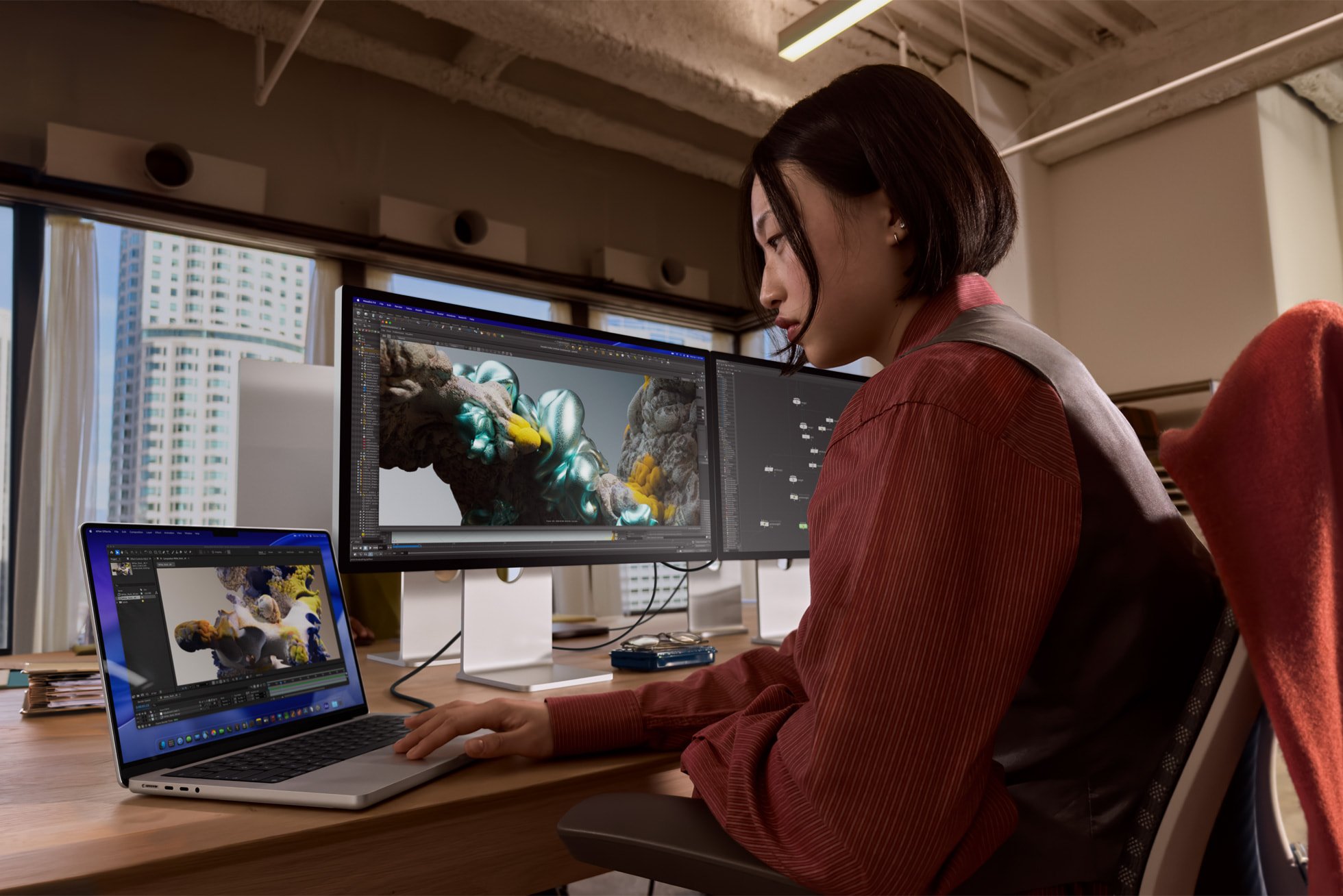 A woman working on a MacBook Pro, powering two high-resolution external displays.