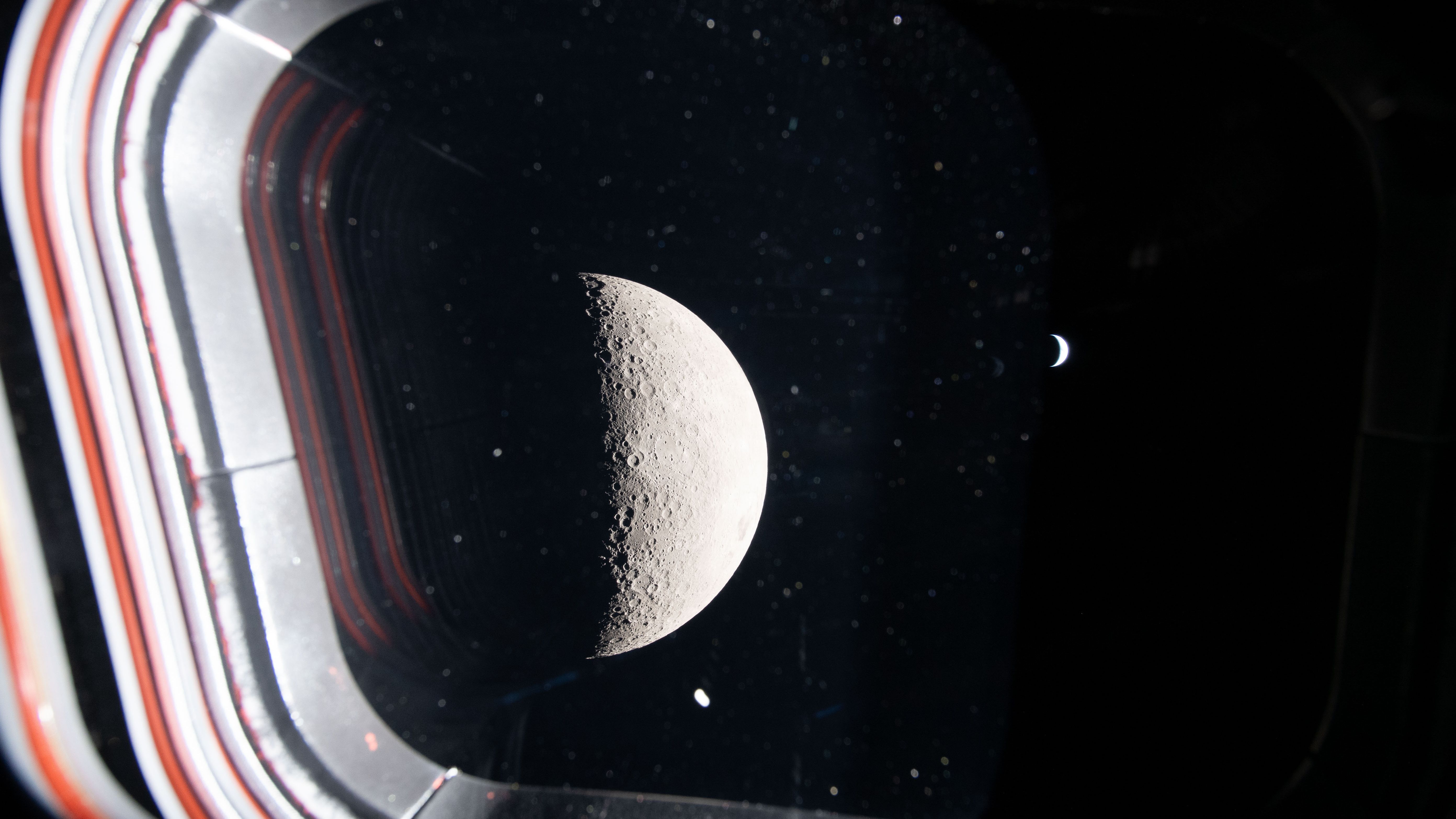 the half moon and a crescent Earth shine through the window of a spacecraft.