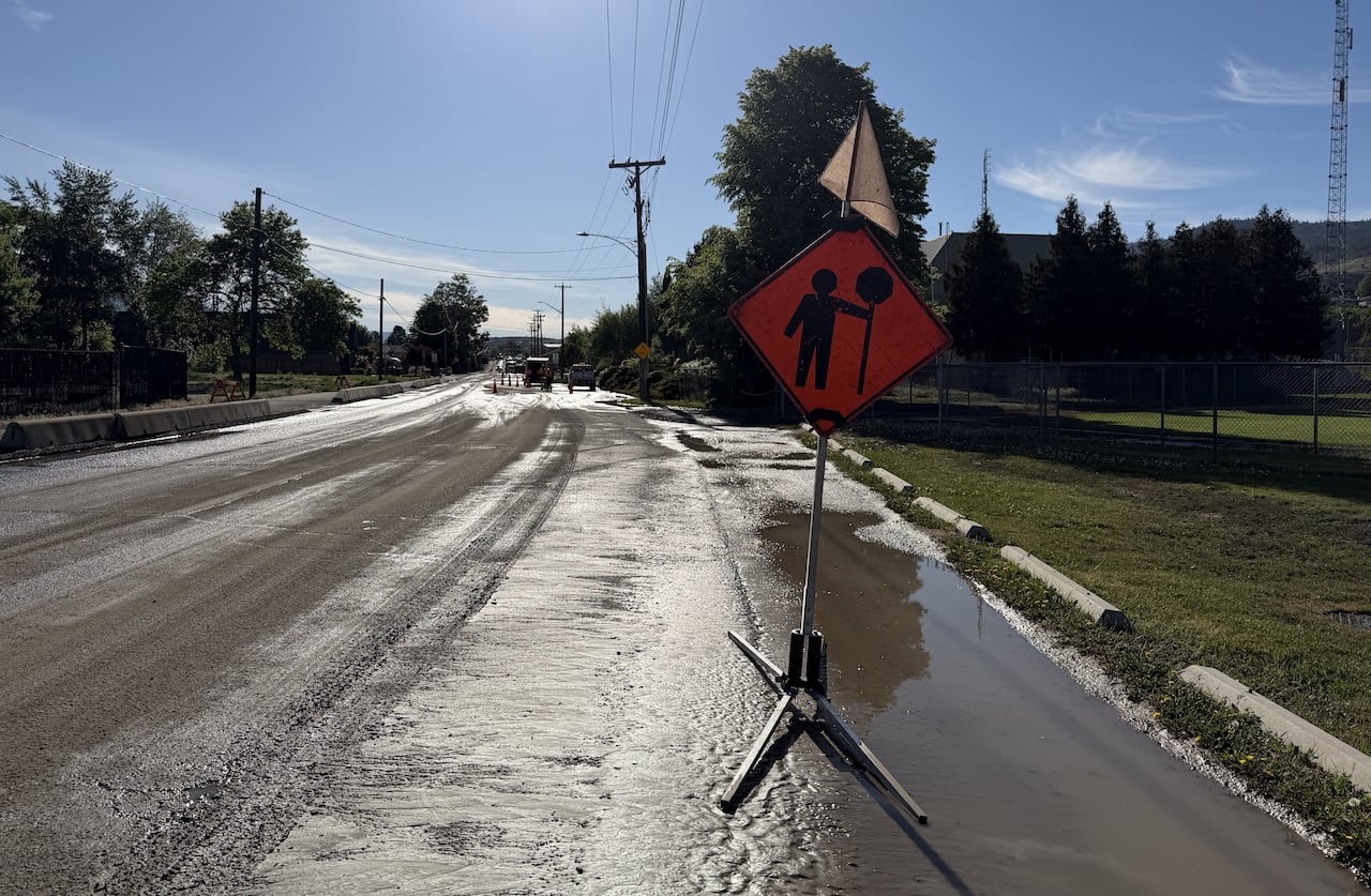 Orange traffic sign sits on a partially flooded roadway.
