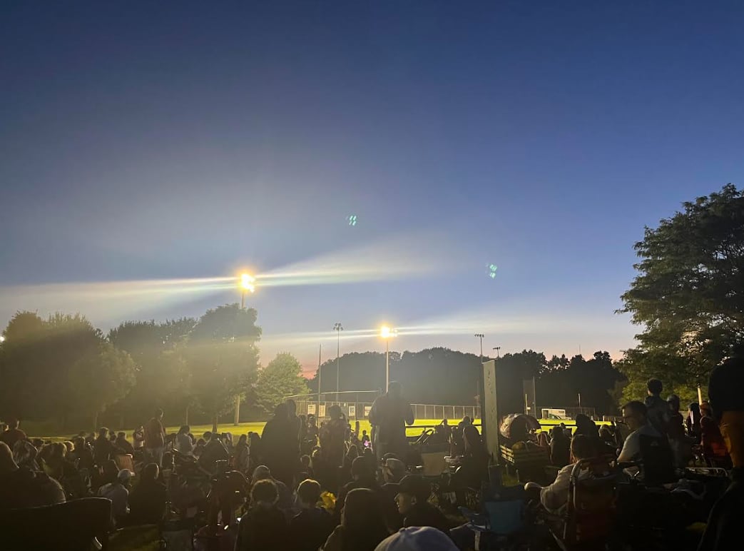 A crowd sitting in lawn chairs at dusk in a park