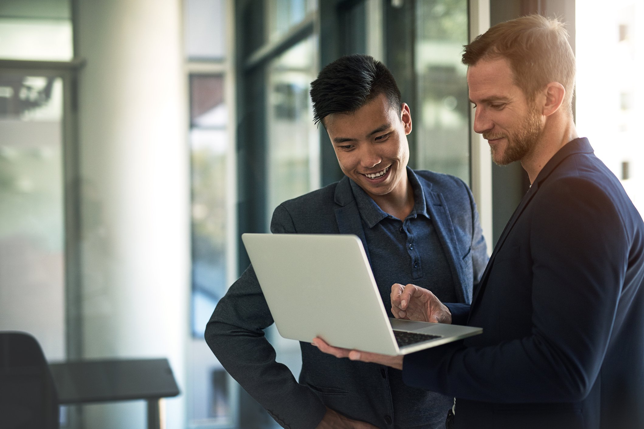Two investors, standing in an office, look at something on a laptop.