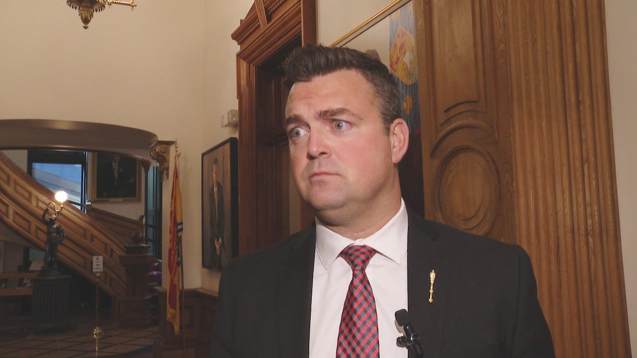 A man in a tie stands in a legislative building.