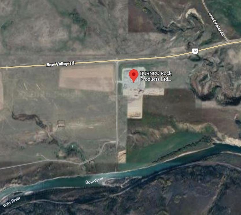 An aerial view shows a gravel pit in the southeast corner of the intersection of Bow Valley Trail and a range road, with the Bow River to the south.