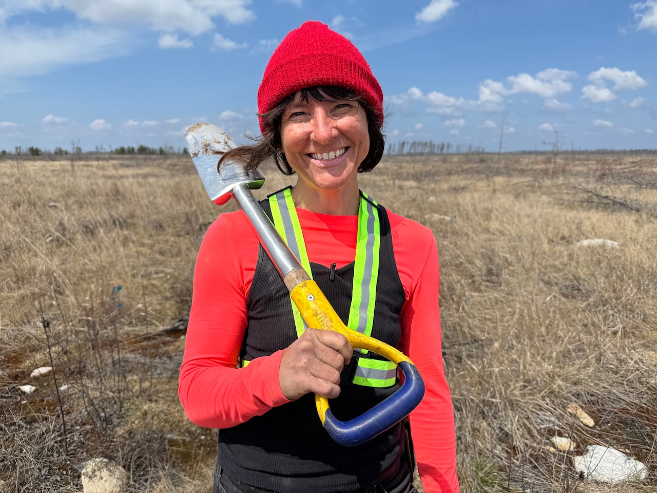 woman standing in a field with a shovel over her shoulder