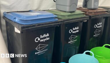 Four black bins with different coloured lids are lined up inside a tent during an event. Small grey food caddie bins sit on top of the bins.