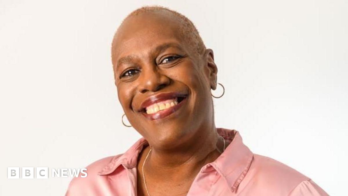 A woman with short hair, hoop earrings and a pink shirt smiling at the camera.