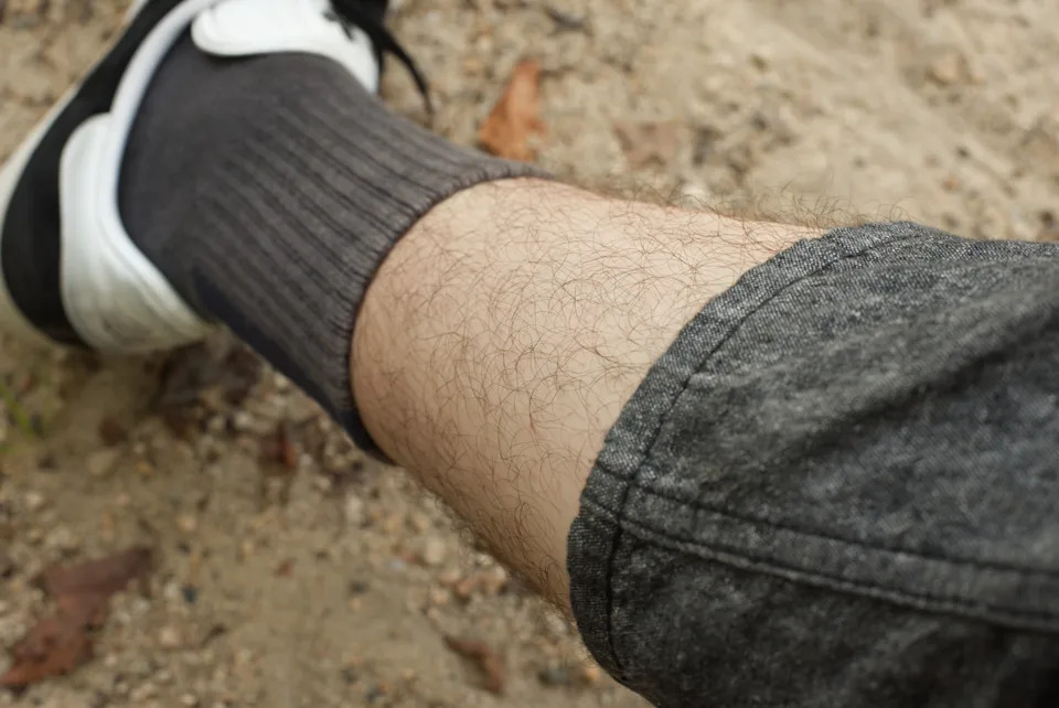 Person wearing gray socks and white sneakers with gray pants sits on sandy ground