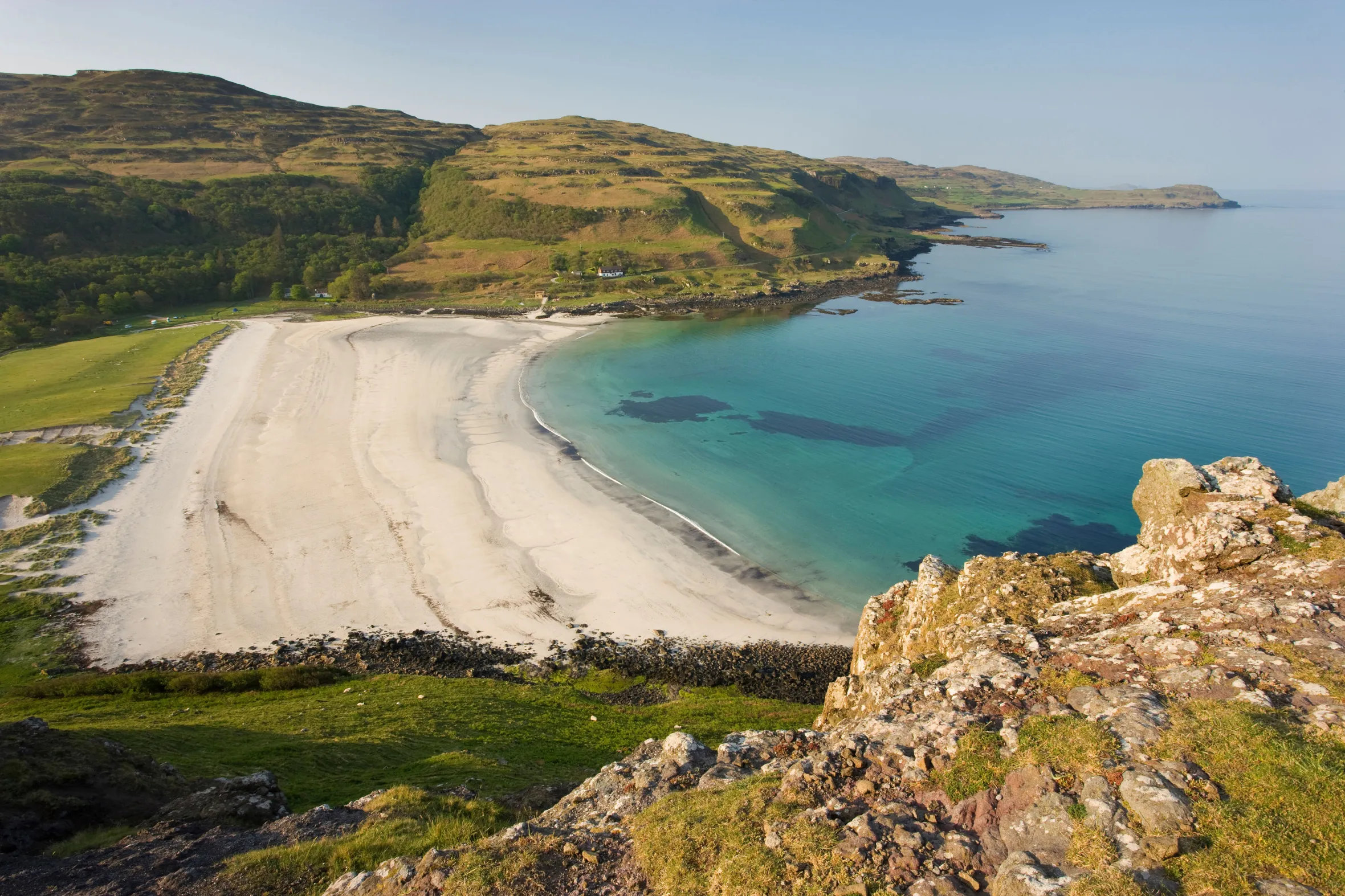 Aerial view of Calgary Bay in the Isle of Mull, Scotland, showing a white sand beach, turquoise water, and green hills.