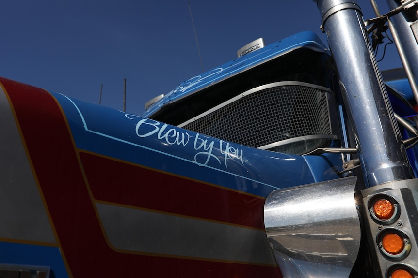 A phrase "blew by you" is written in white cursive script near the front of a blue and red truck.