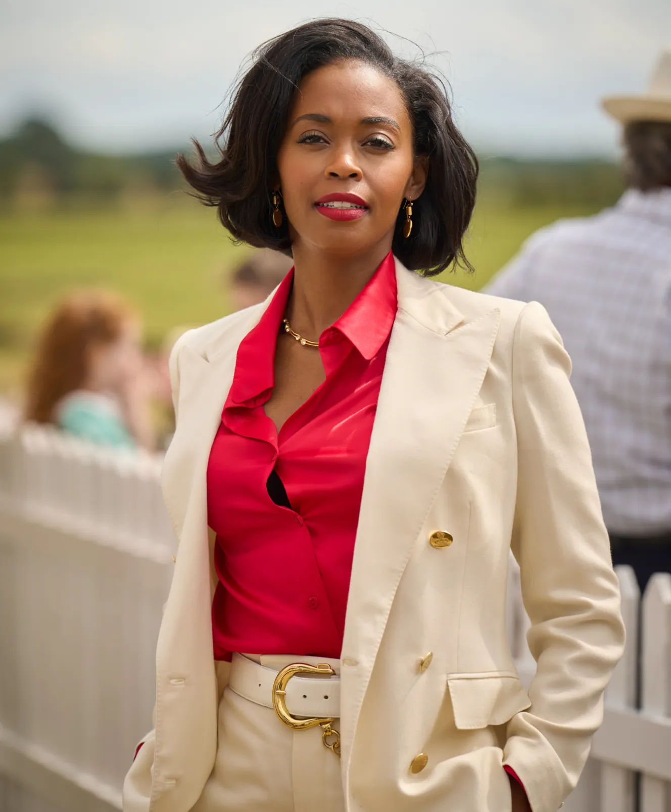 A woman in a red shirt and cream suit jacket with a gold belt buckle.