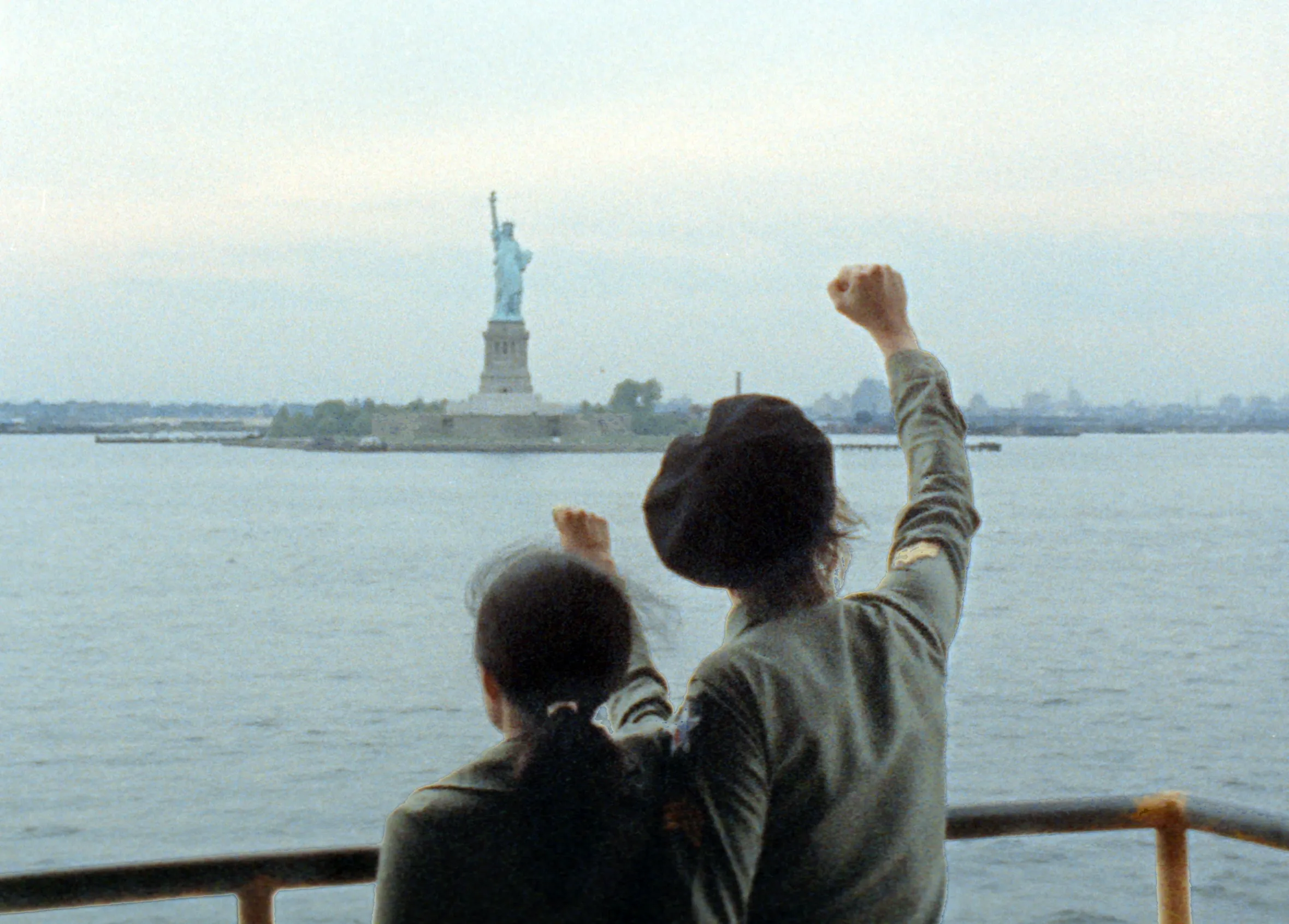 John Lennon and Yoko Ono raise their fists in front of the Statue of Liberty.