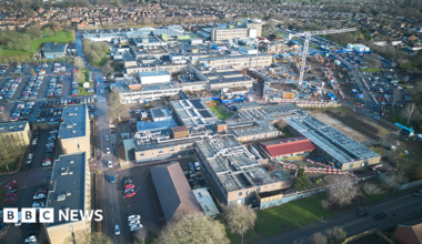 An aerial view of a hospital site with a number of large buildings surrounded by car parks and grassy areas