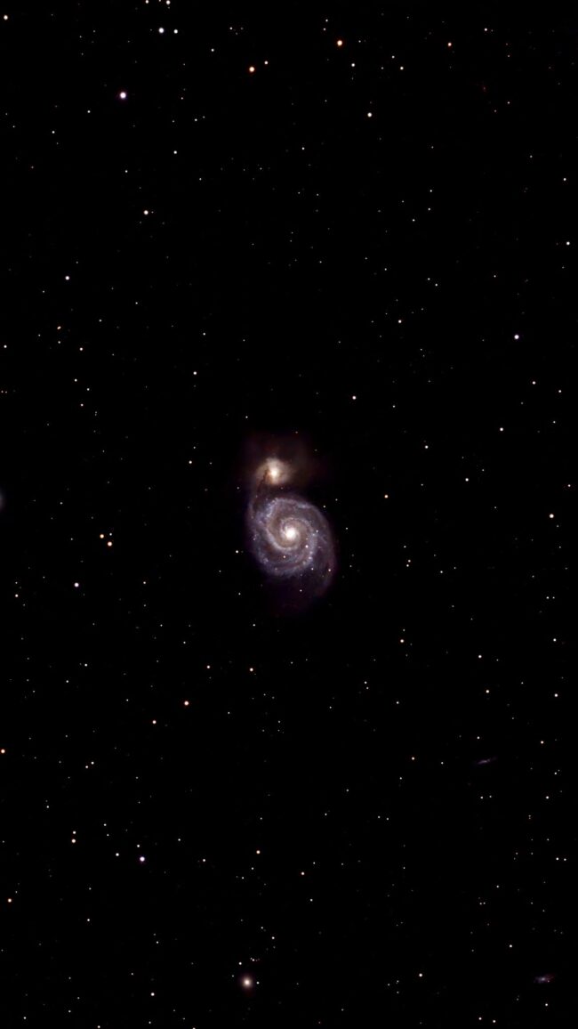 A yellowish spiral galaxy, seen head-on, with a foreground of sparse bright stars.