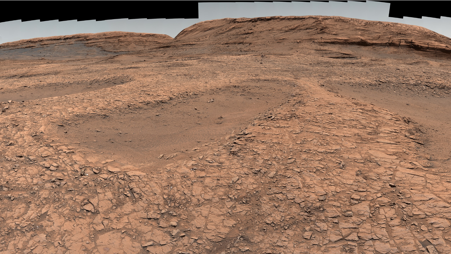photo of mars taken by a rover, showing a rocky desert in the foreground and a mountain in the background