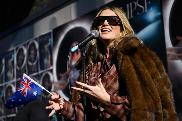 Delta Goodrem holding an Australian flag, smiling as she sings into a microphone.