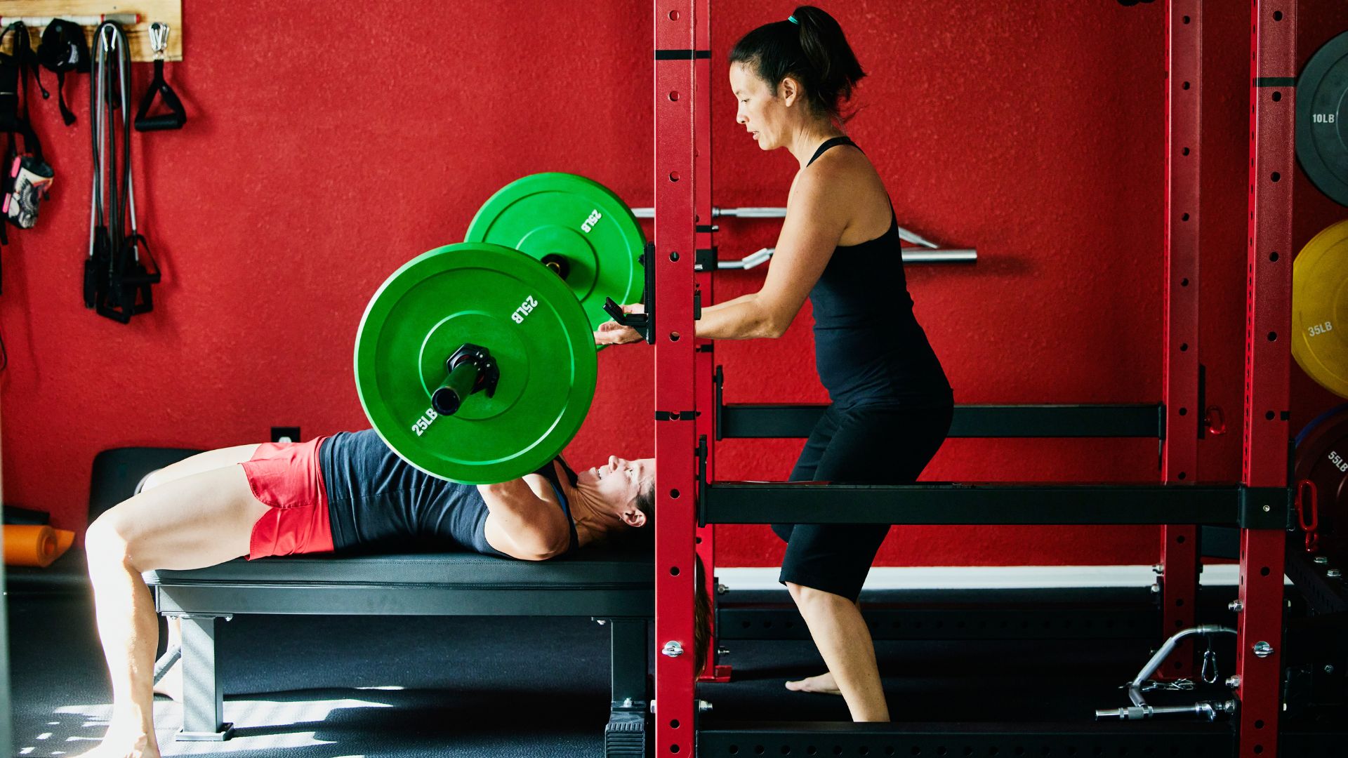 Woman lifting weights on barbell in chest press exercise with PT standing behind for support