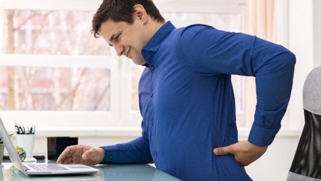 man holding his lower back in pain while sitting at work
