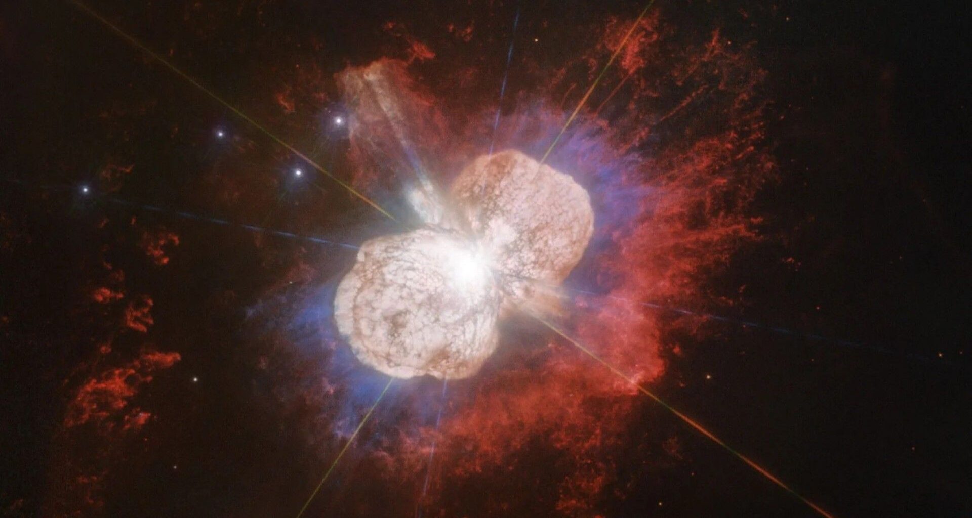 two large lobes of colorful gas radiate outward from a bright pinpoint of light