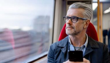 Thoughtful man using his phone while riding on a train and looking through the window