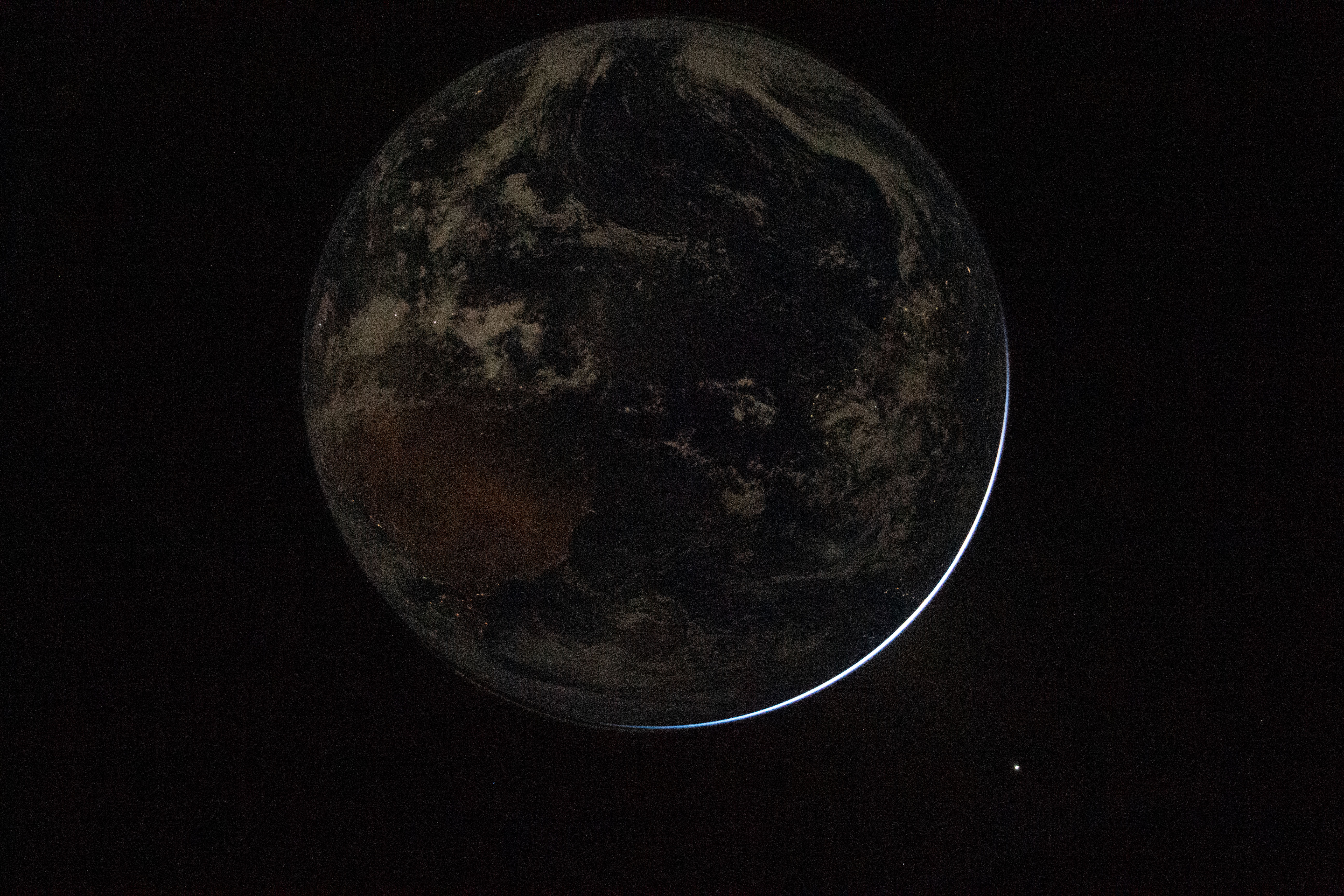 a sliver of light shines around the edge of a darkened night side Earth