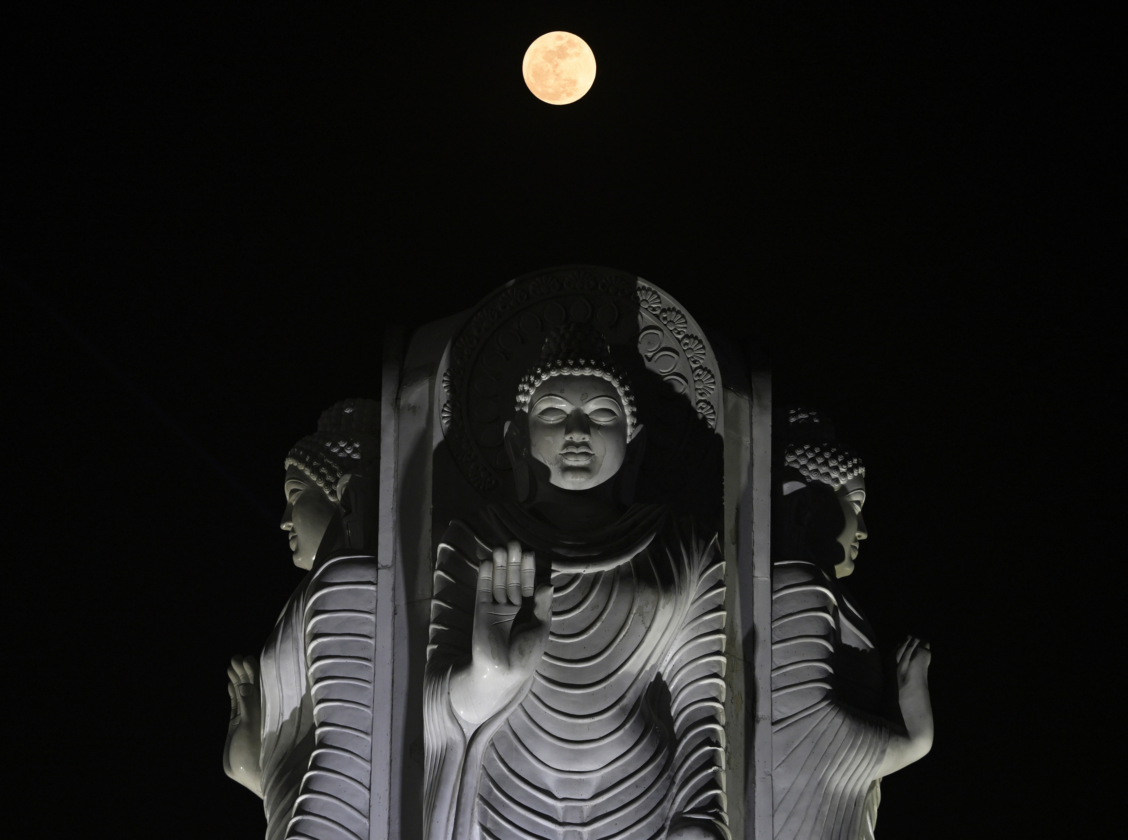 A full moon shines above a statue of Lord Buddha at night.